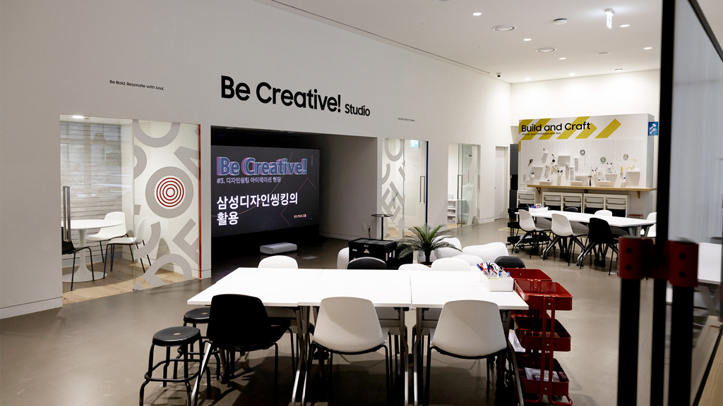 A black sign on a white wall that reads Be Creative! Studio. This is the lobby of a conference room with a large table in the center.