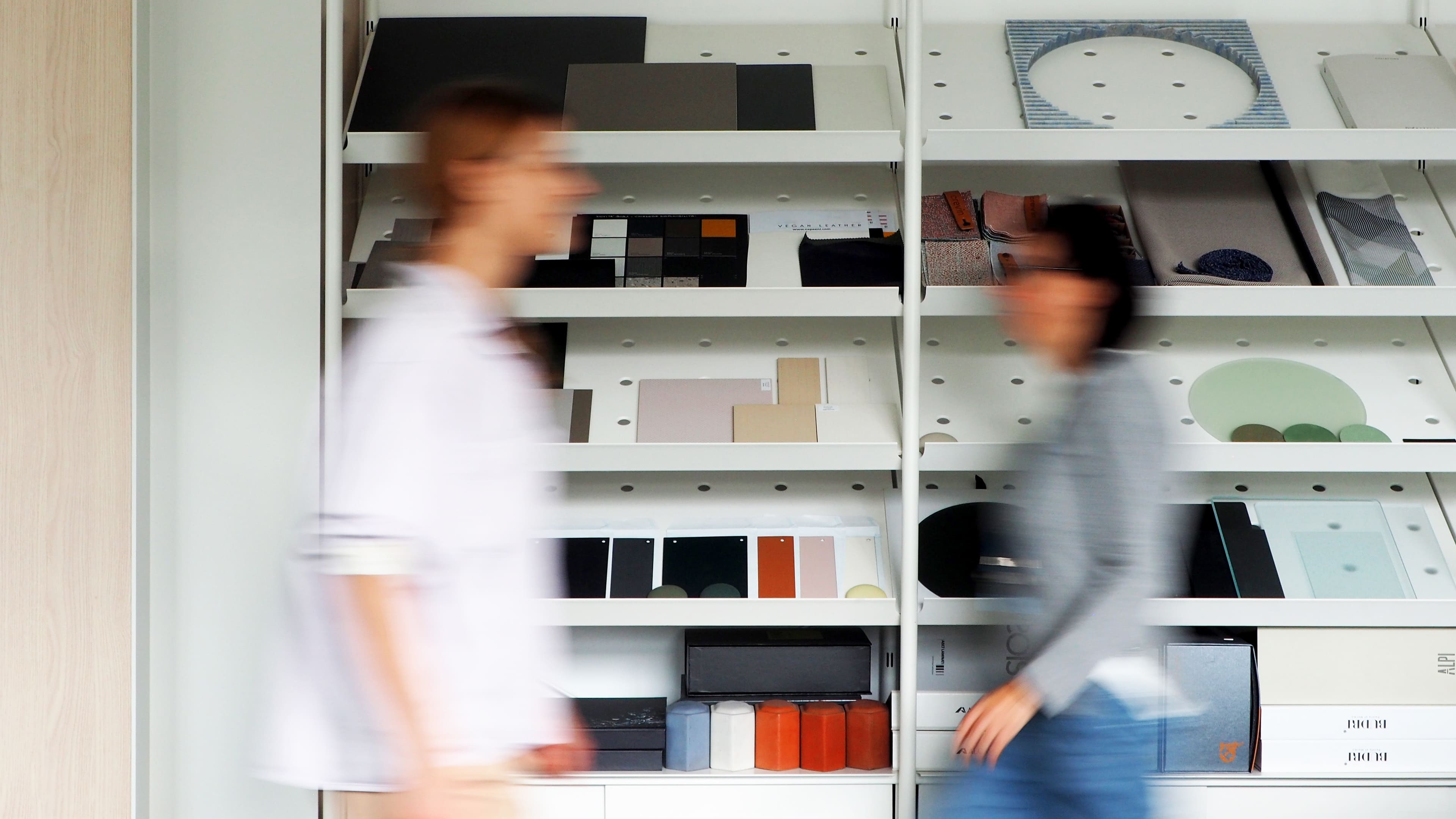 People move swiftly past shelves filled with design materials, where dynamic motion meets organized space, creating a vibrant and creative atmosphere