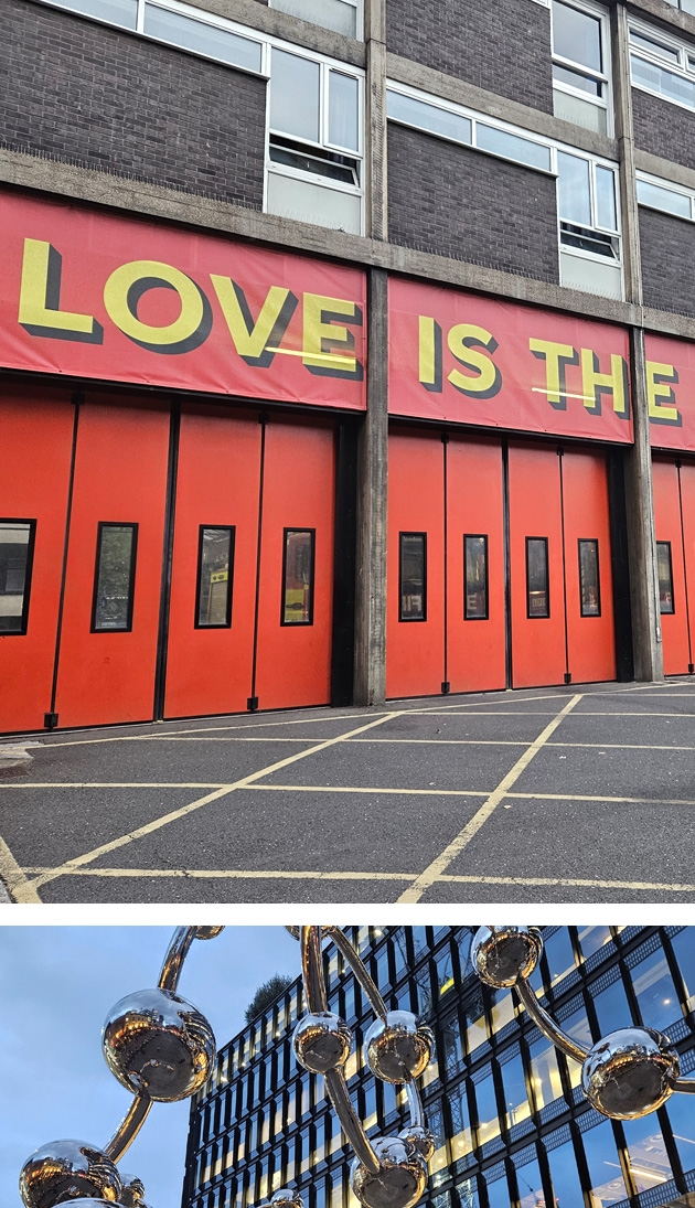 The building facade features bold red doors with the striking phrase 'LOVE IS THE' displayed above, infusing the space with vibrant energy and meaning. Shimmering metallic spheres interconnected in a striking structure stand out against the modern building backdrop, symbolizing a fusion of science and art in its unique design.