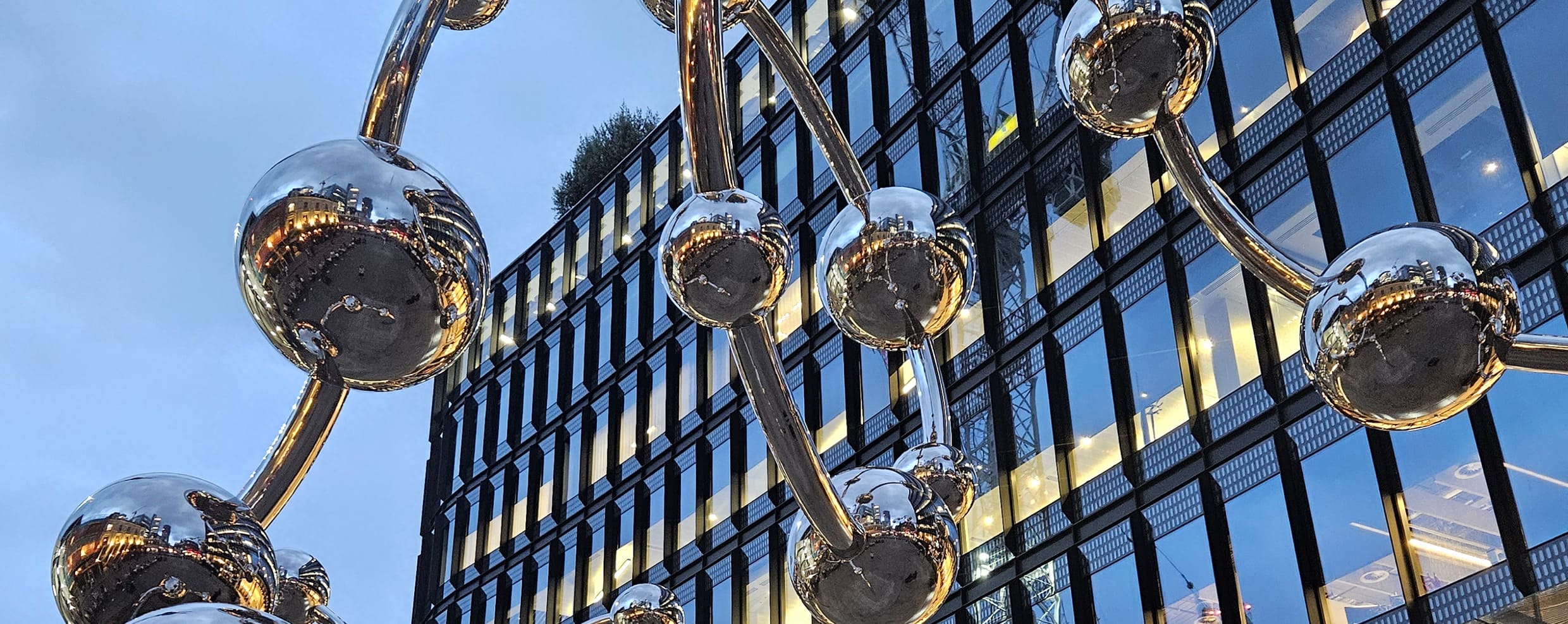 Shimmering metallic spheres interconnected in a striking structure stand out against the modern building backdrop, symbolizing a fusion of science and art in its unique design.