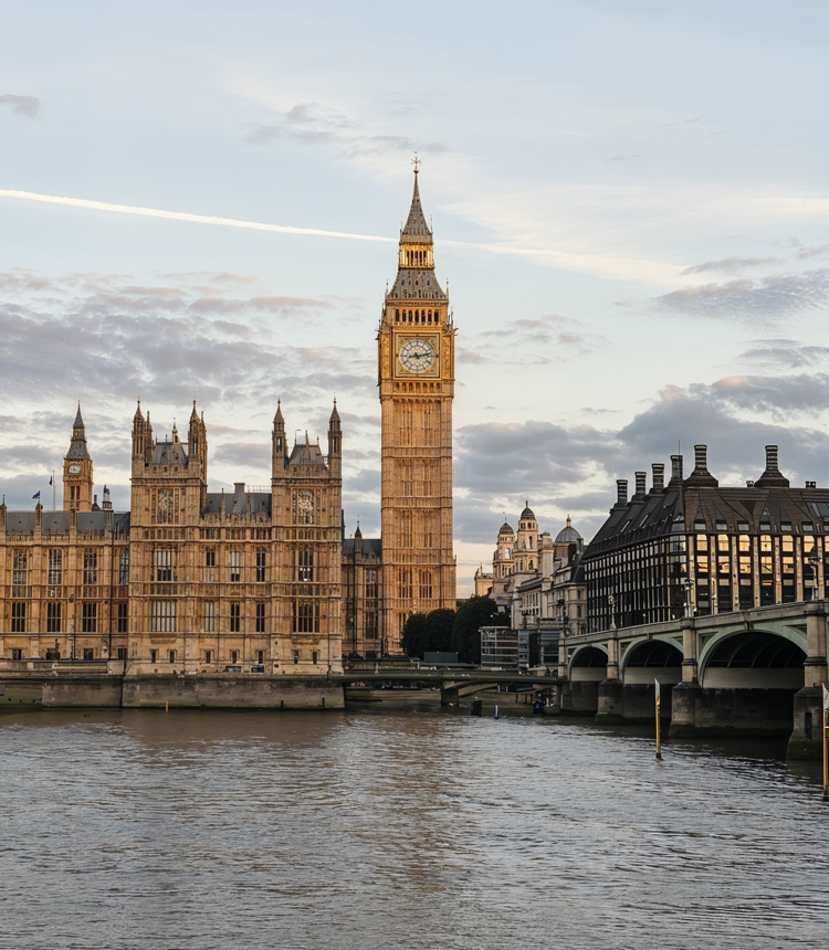 London's iconic Big Ben and the Palace of Westminster stand majestically by the riverside under the twilight sky. The historic and grand architecture captures the eye.