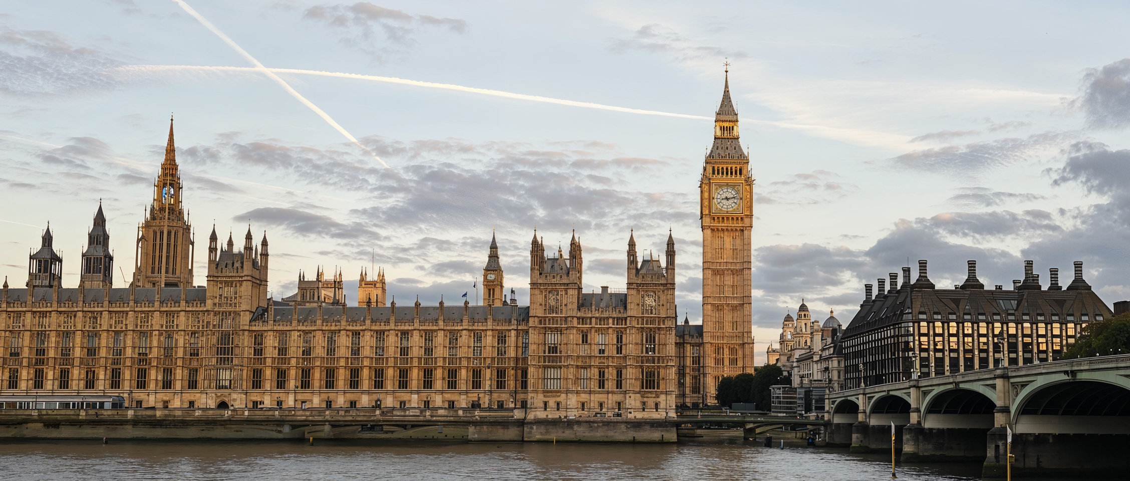 London's iconic Big Ben and the Palace of Westminster stand majestically by the riverside under the twilight sky. The historic and grand architecture captures the eye.