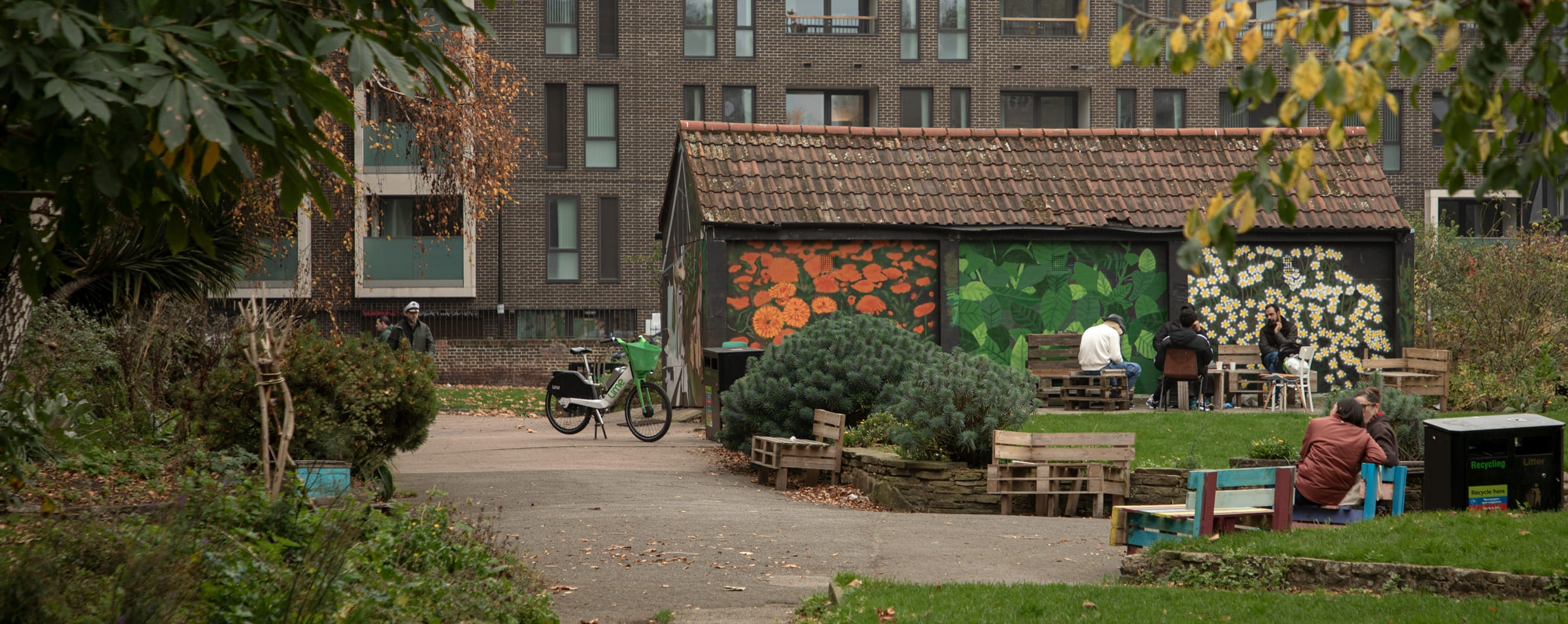 A small garden featuring a colorful mural-adorned hut and surrounding benches creates a warm and inviting community space.