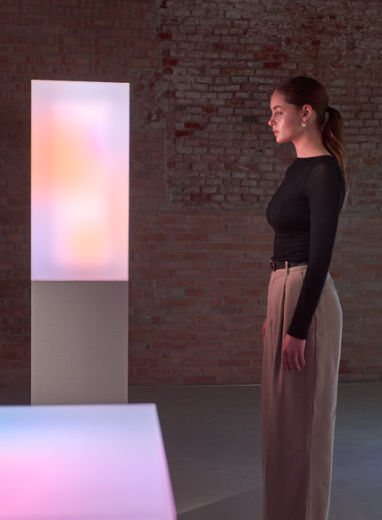 A white woman is looking at a glowing art installation that displays vibrant colors.