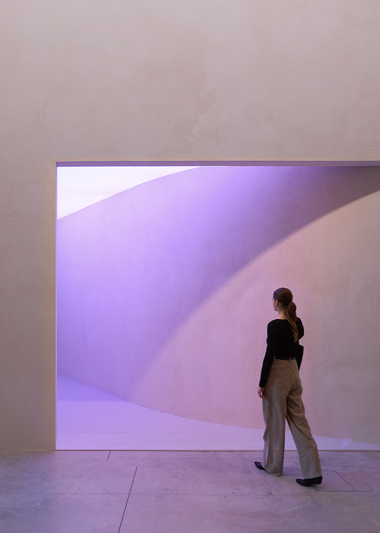 There is a door on a huge yellow wall, and purple light is leaking out. A young woman is walking toward the door.