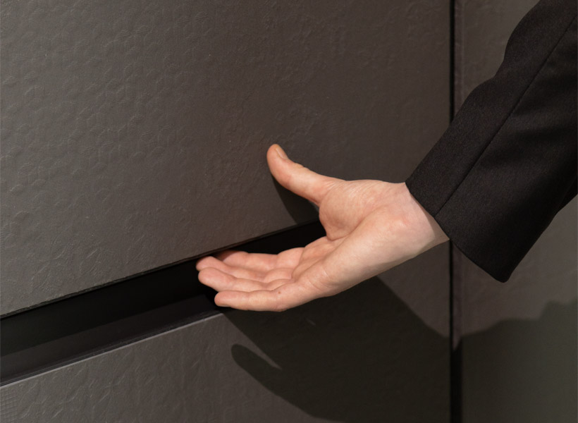 Close-up of an open palm gesture where a hand in black sleeves posed to close a textured dark gray Bespoke door.