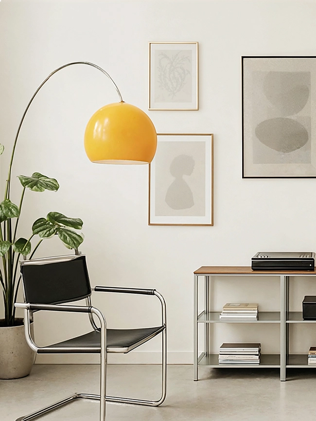 A modern living room interior featuring a metal-framed shelf with a wooden top holding audio equipment, a lamp, books, and vases. A black leather chair and a potted plant are placed on the left side.