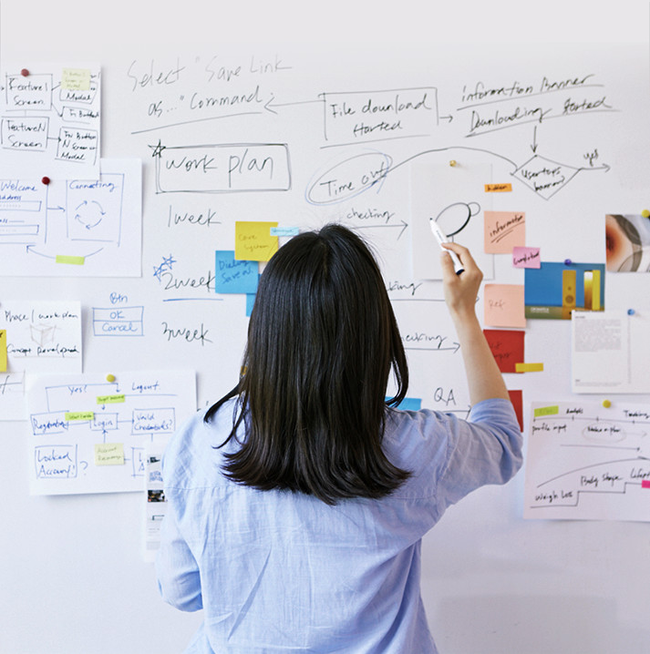 A designer writes on a whiteboard with sticky notes and materials attached to it.