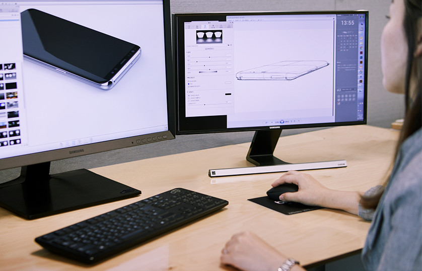 A designer looks at a sketch of a cellphone and renders the image on a computer monitor.