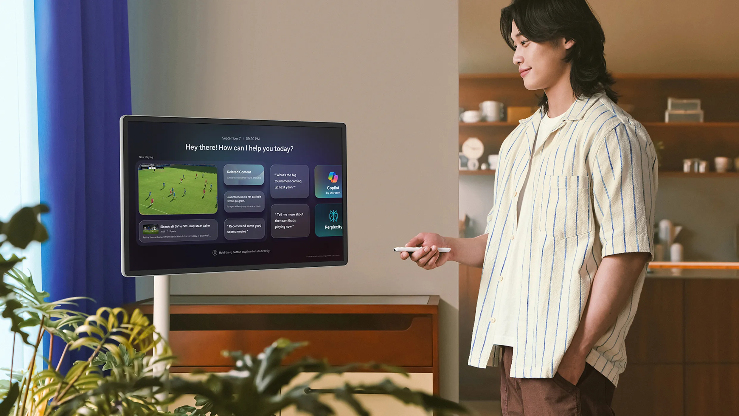 A man watching a movie in the living room with Samsung Display Moving Style. He holds a remote while looking at the screen, which shows a film scene along with the menu interface.