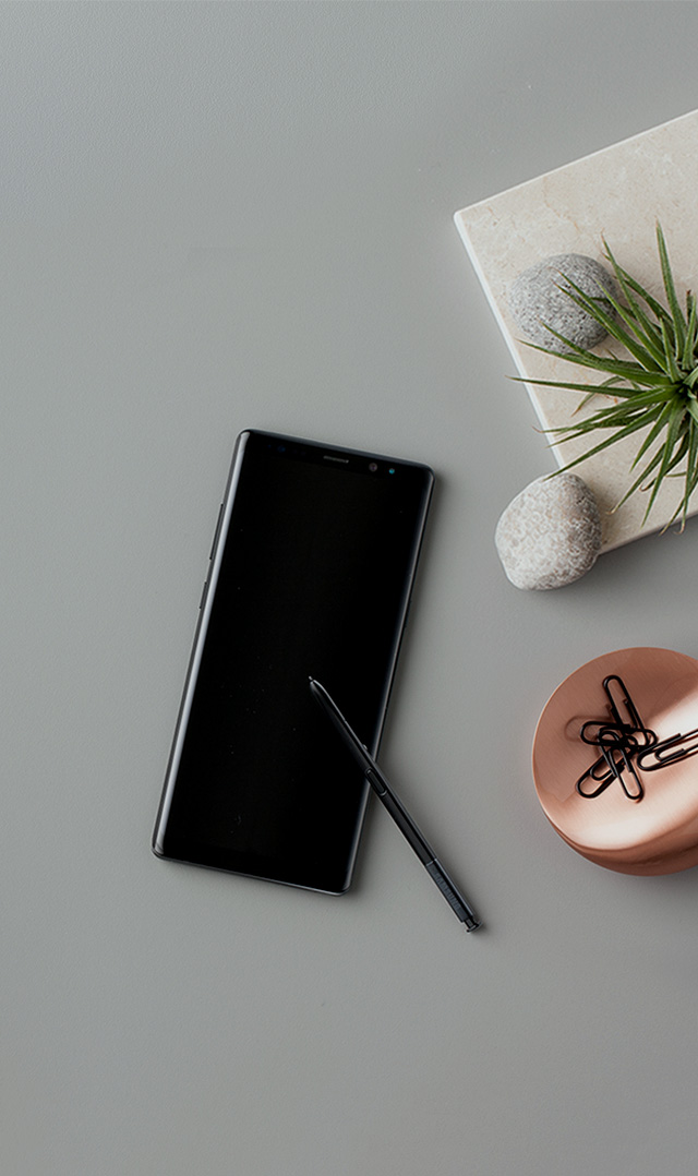 Samsung Galaxy Note 8 is placed on a table with plants, paperclips, candles, etc.