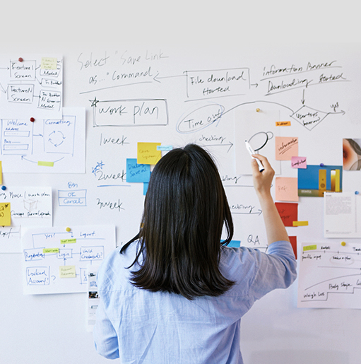 A designer writes on a whiteboard with sticky notes and materials attached to it. 