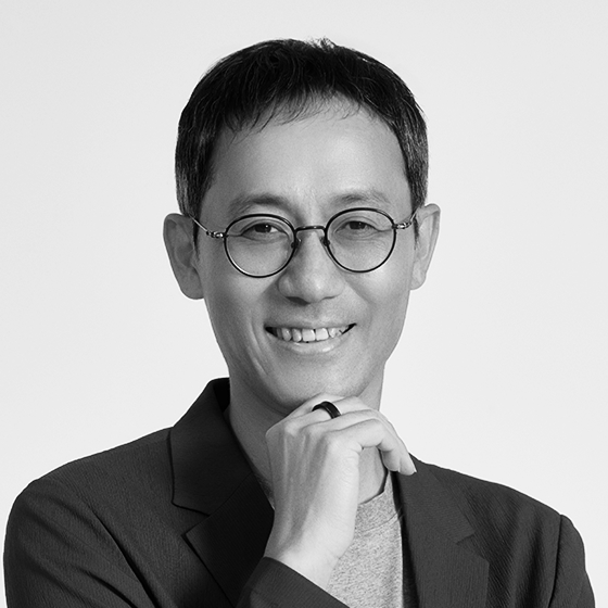 안경을 쓰고 턱에 손을 올린 채 웃고 있는 남성.